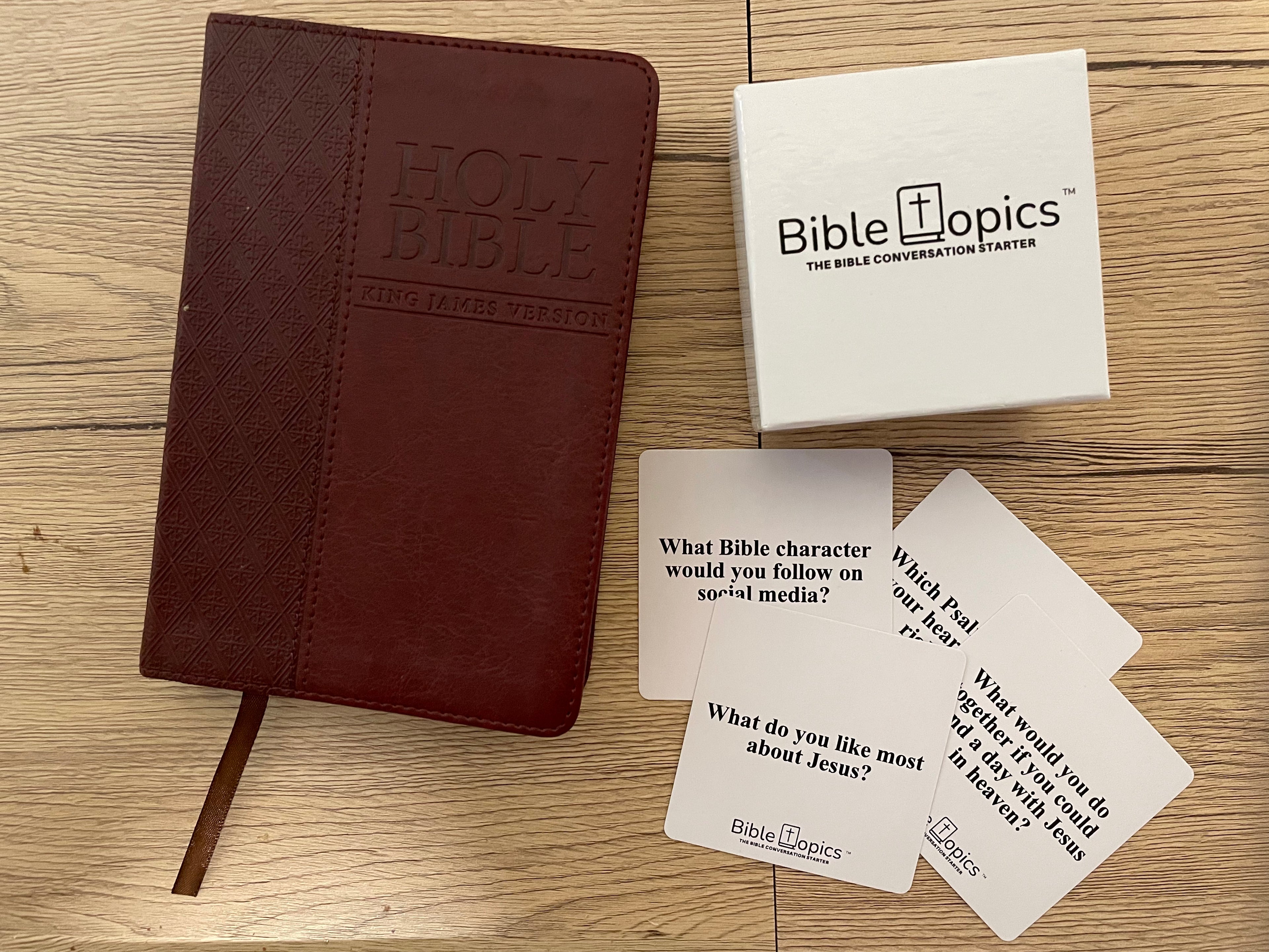 Brown Bible, white box labeled 'Bible Topics', and three question cards on a wooden surface.